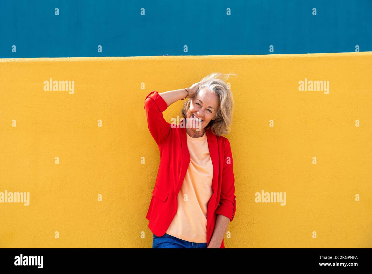 Happy woman with hand in hair wearing red blazer Stock Photo