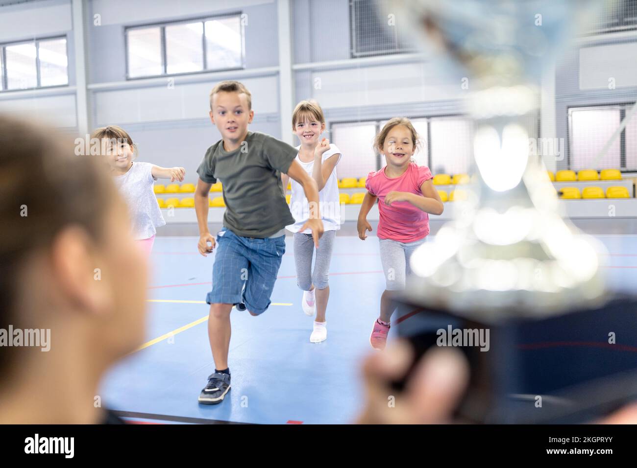Excited students running towards trophy held by teacher at school sports court Stock Photo