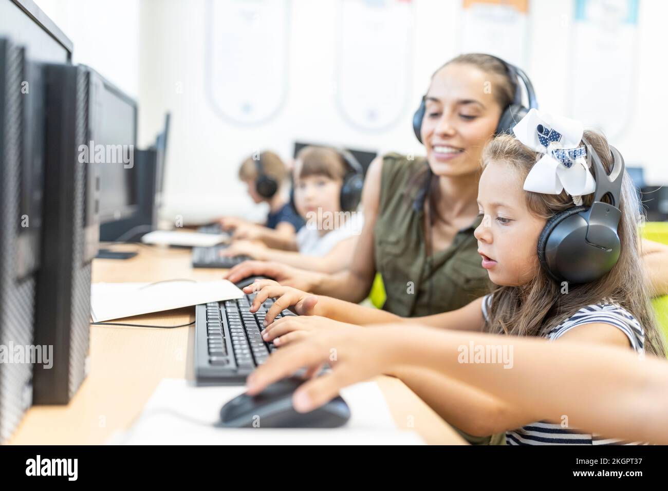 Girl wearing headphones using computer with teacher in class at school Stock Photo