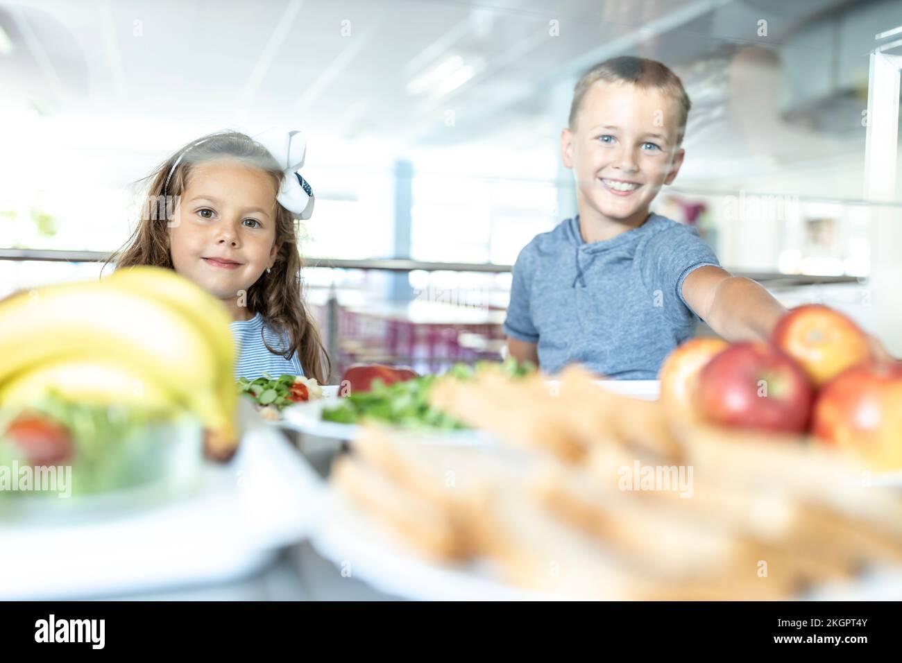Smiling elementary students taking fruits at lunch break in school cafeteria Stock Photo