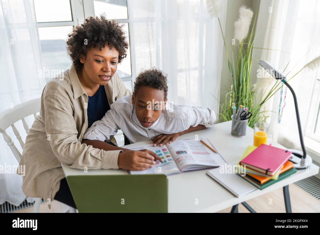 Mother assisting son doing e-learning through laptop on table at home Stock Photo