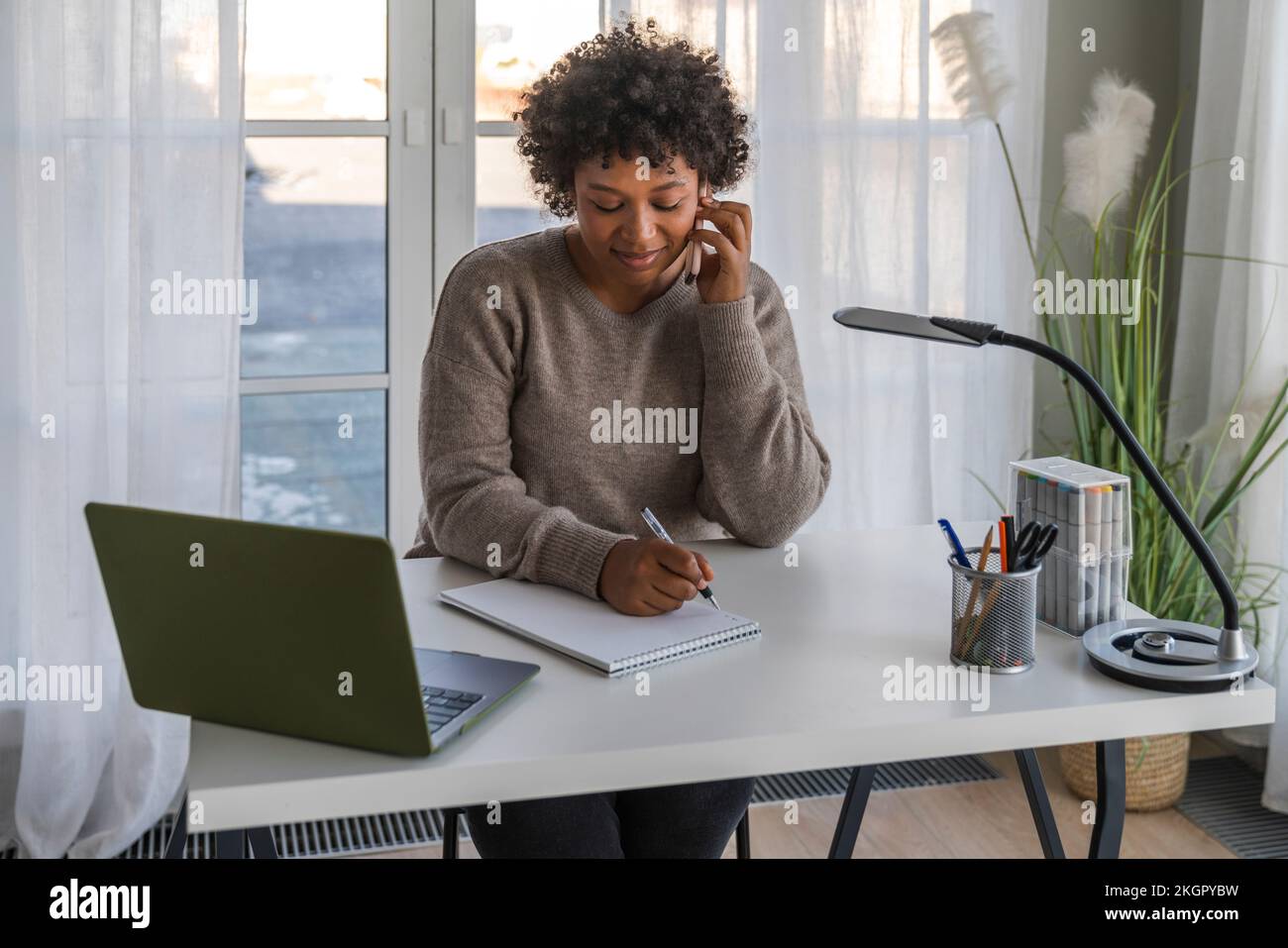 Freelancer talking through smart phone and taking down notes at home Stock Photo