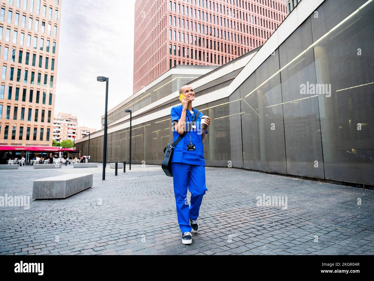 Smiling nurse talking over mobile phone and walking on footpath Stock Photo