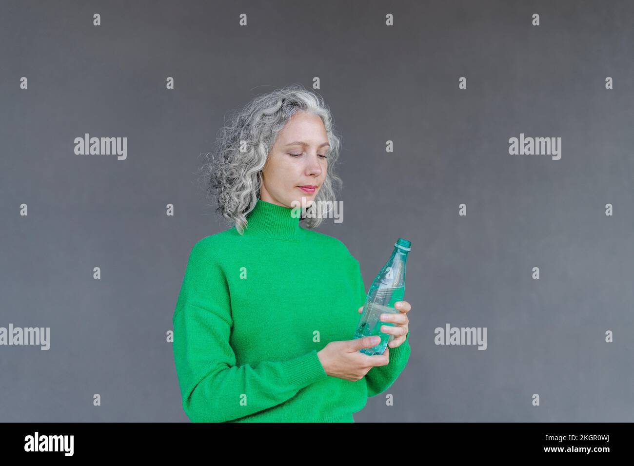 Woman with gray hair holding green water bottle in front of wall Stock Photo