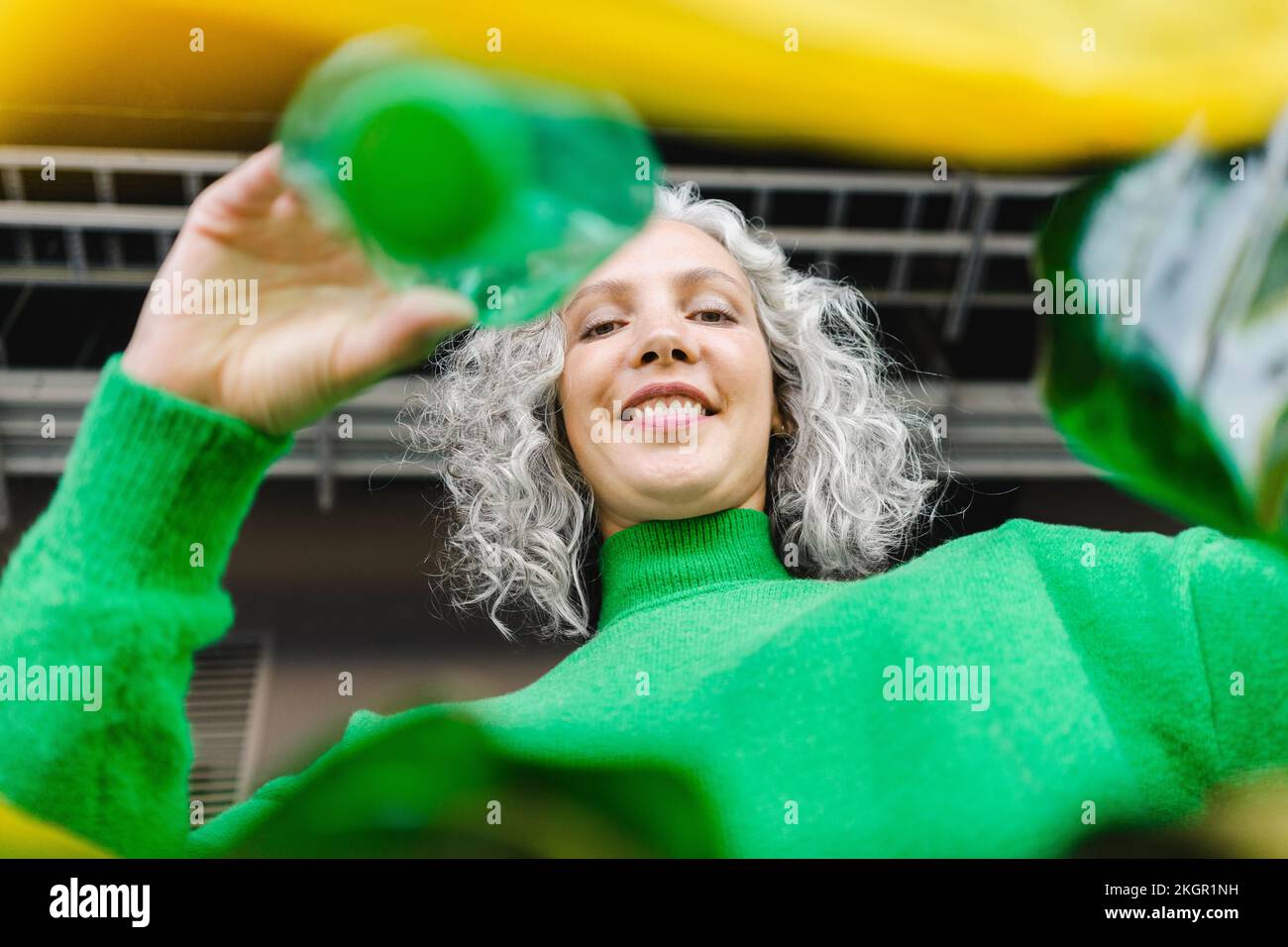 Smiling woman with gray hair putting green bottle in yellow plastic bag Stock Photo Alamy