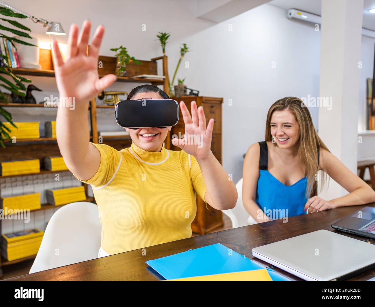 Smiling businesswoman gesturing with VR goggles sitting by friend at table Stock Photo