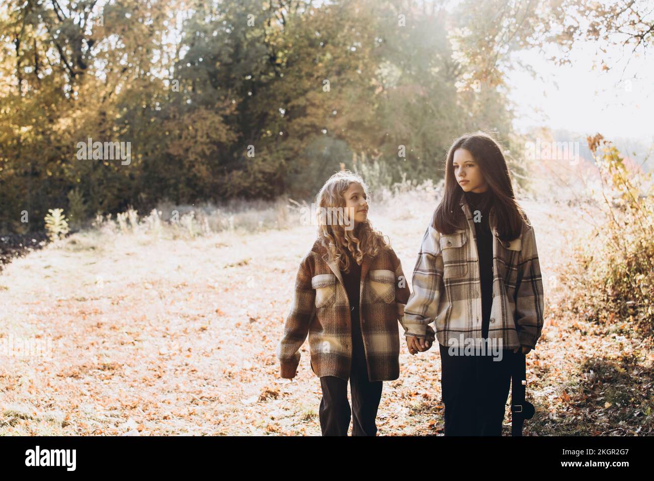 Girl holding hands with sister and walking in forest on sunny day Stock Photo