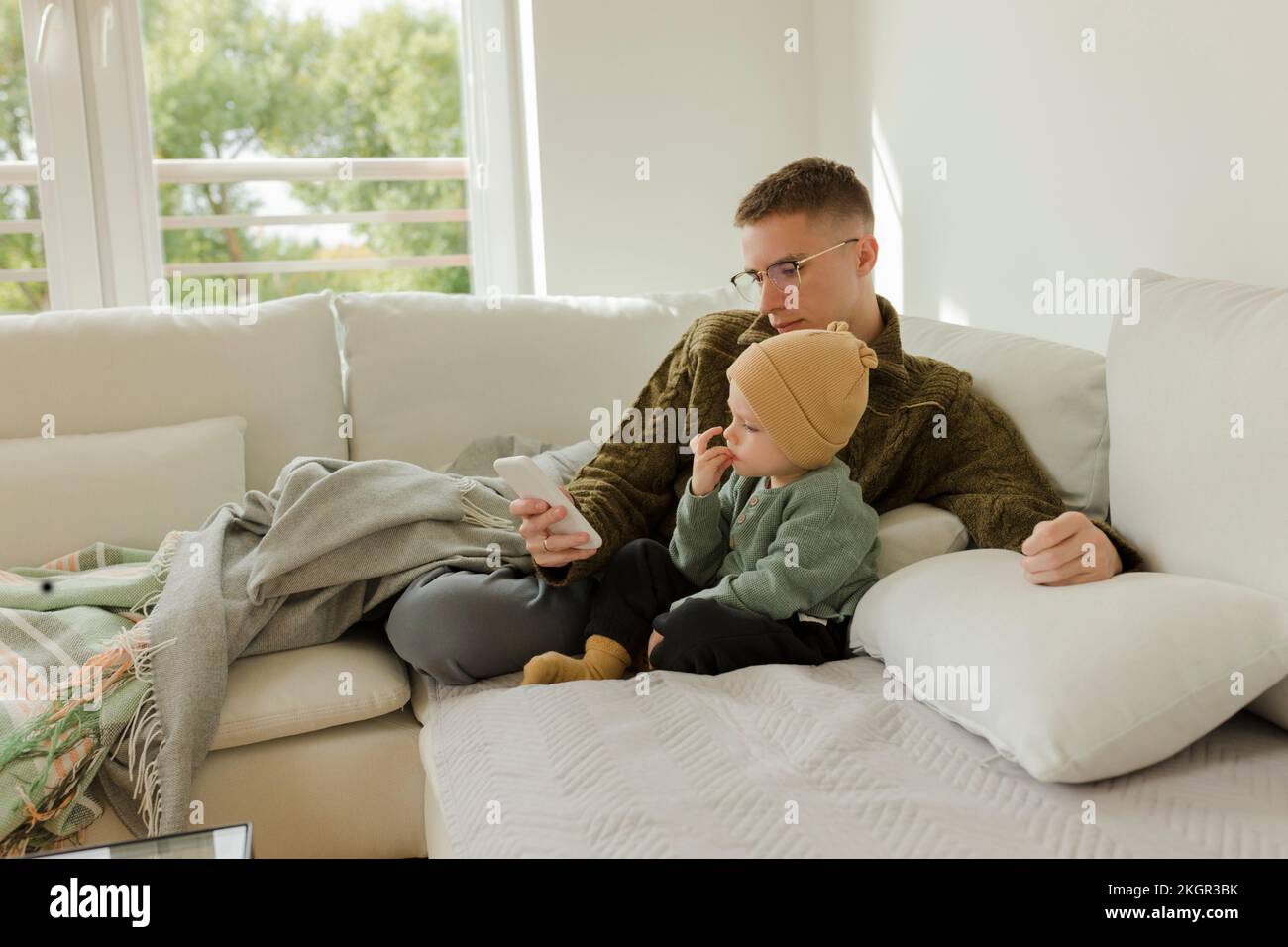 Young man using smart phone with son sitting on sofa at home Stock Photo
