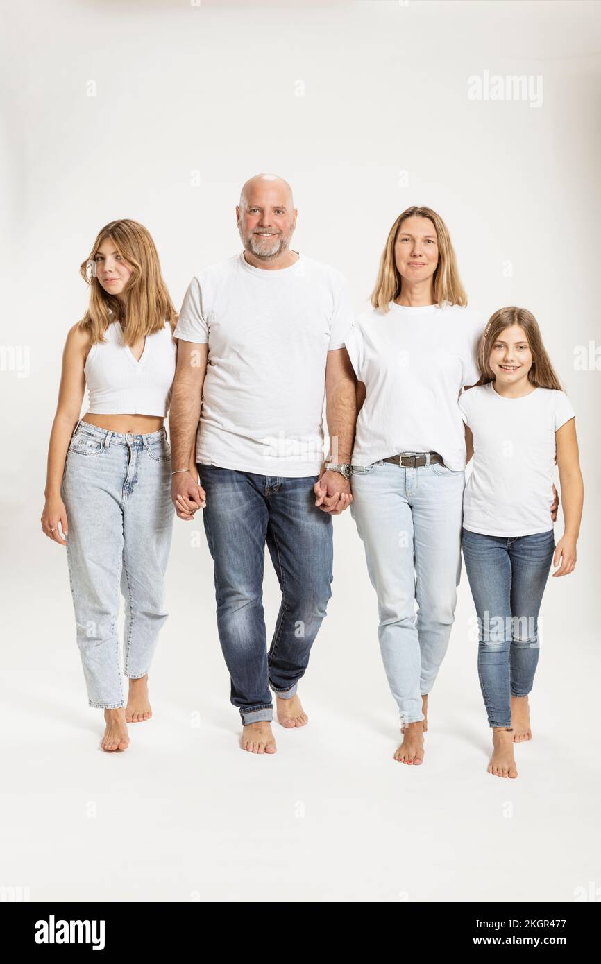 Smiling parents holding hands and walking with daughters in studio Stock Photo