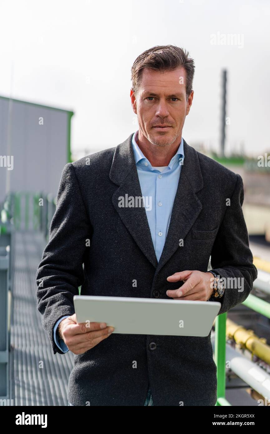 Mature businessman holding tablet PC standing at industrial plant Stock Photo