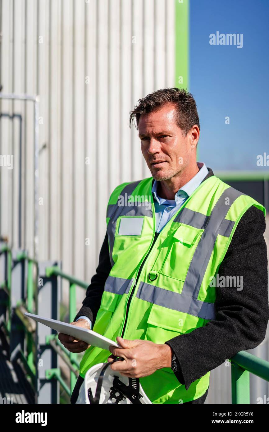 Smiling mature engineer with tablet PC standing by railing Stock Photo