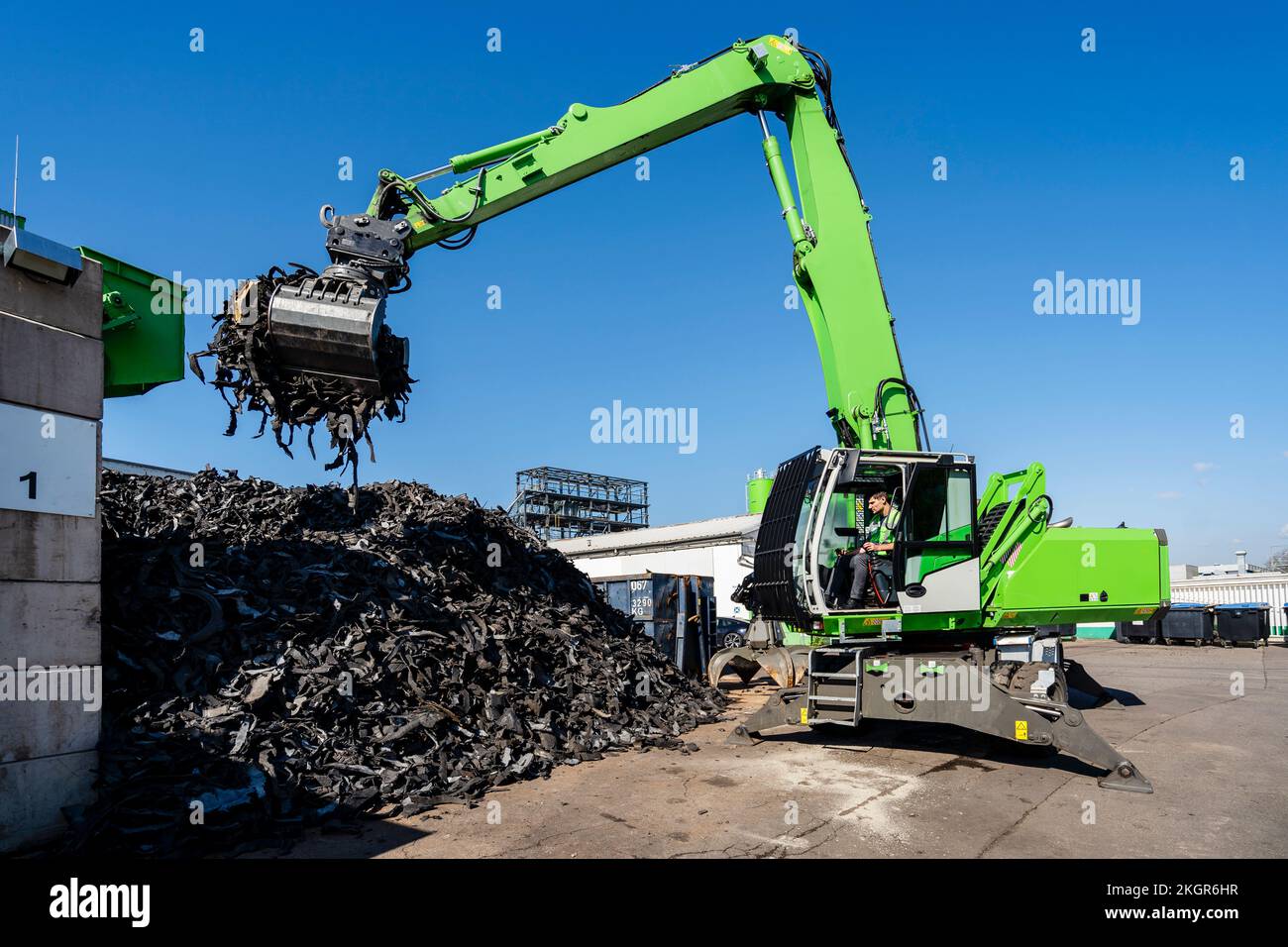 Mature man operating excavator and lifting rubber waste at recycling center Stock Photo