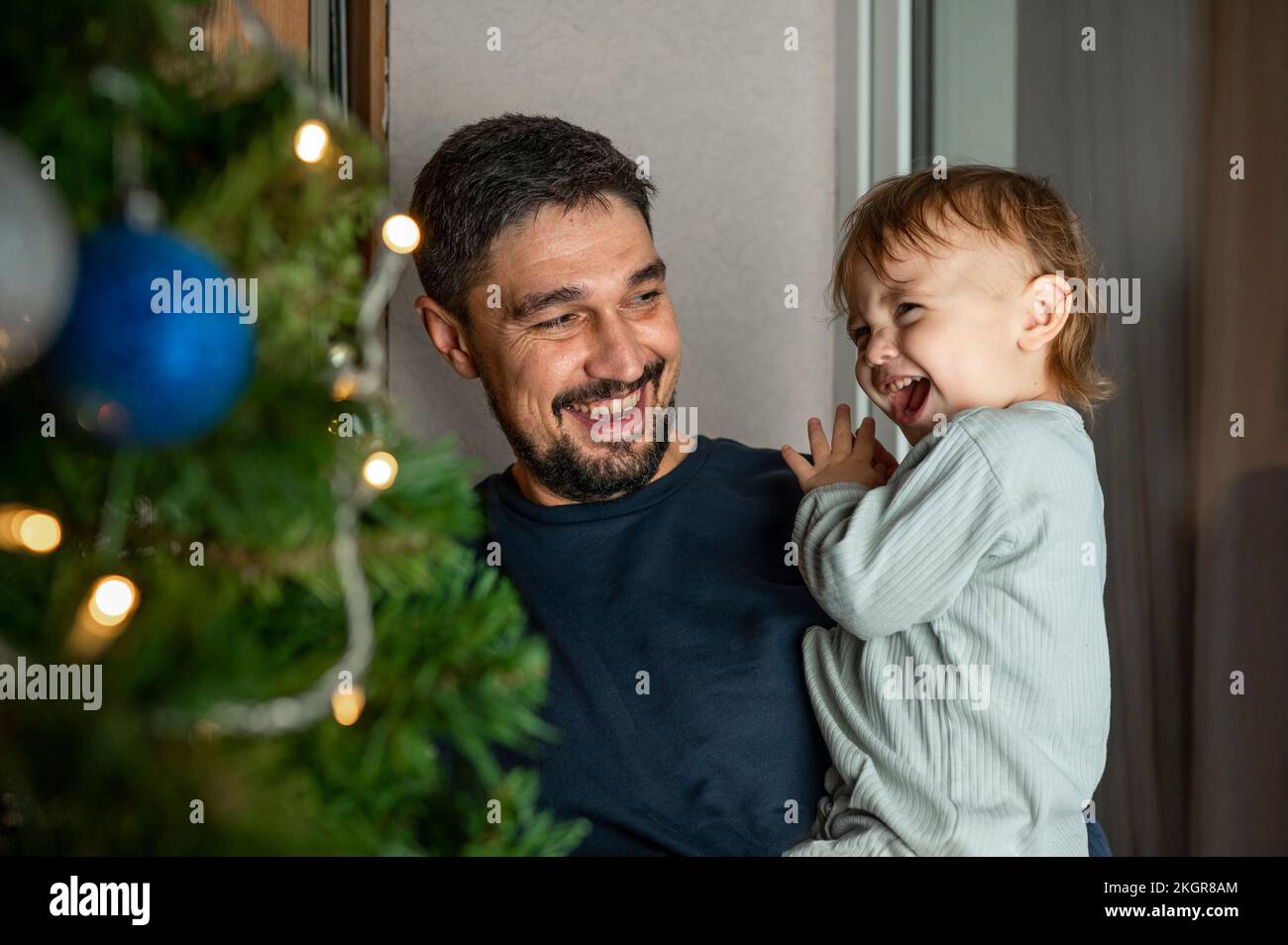 Happy father carrying cute boy in front of Christmas tree at home Stock Photo