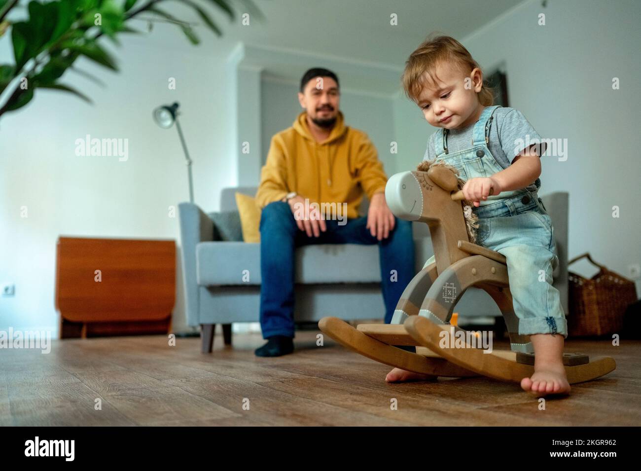 Cute boy playing on rocking horse with father in background Stock Photo