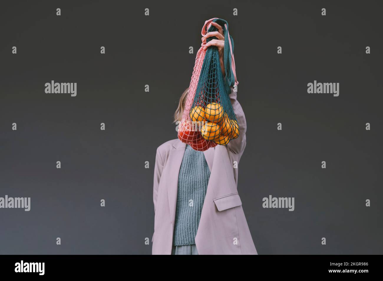Woman covering face with mesh bag in front of gray wall Stock Photo