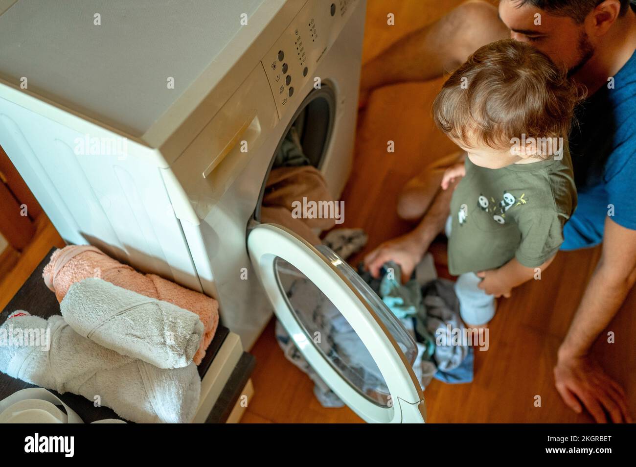 Son with father loading clothes in washing machine Stock Photo