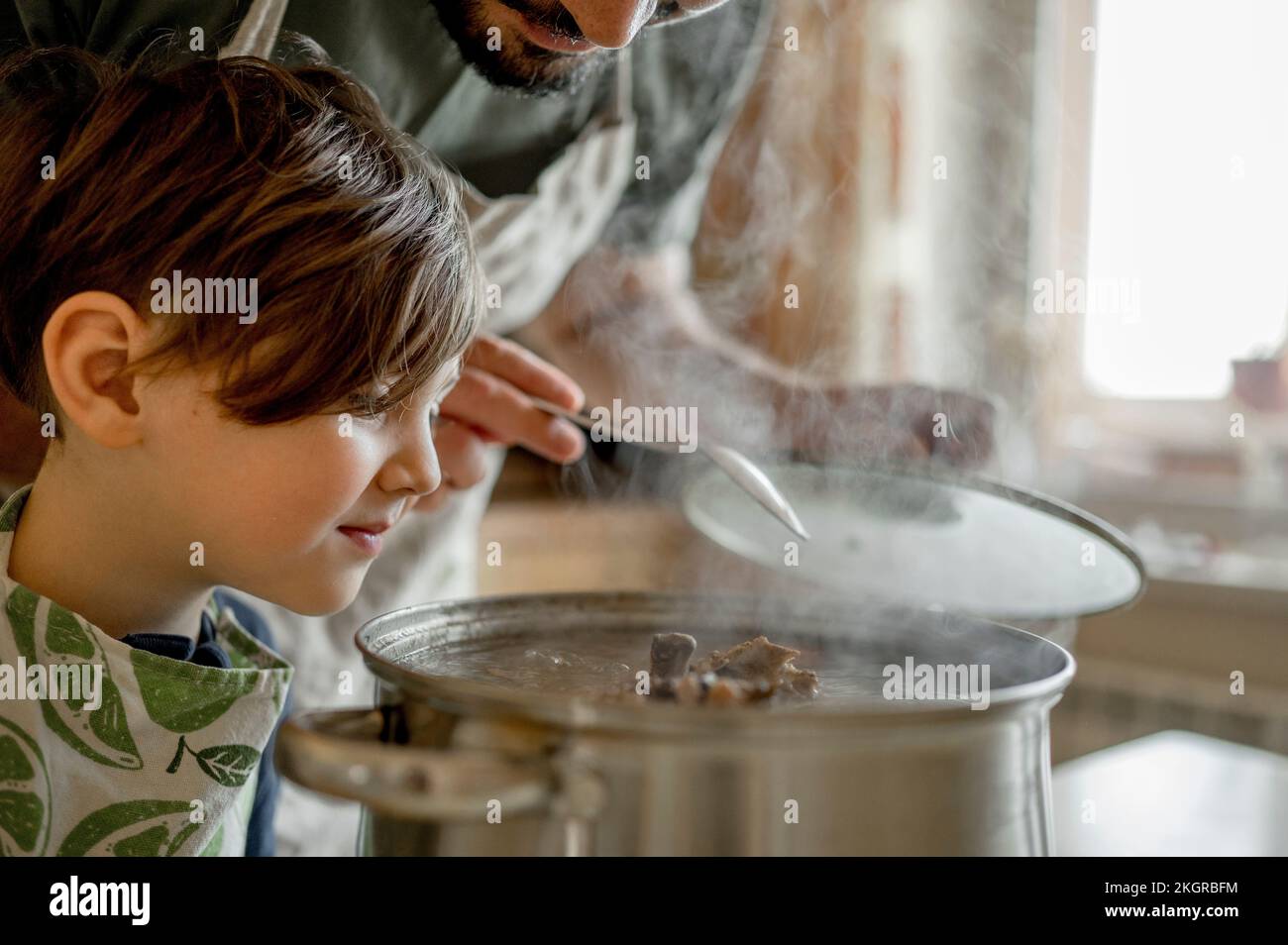 Boy looking at soup prepared by father in kitchen Stock Photo