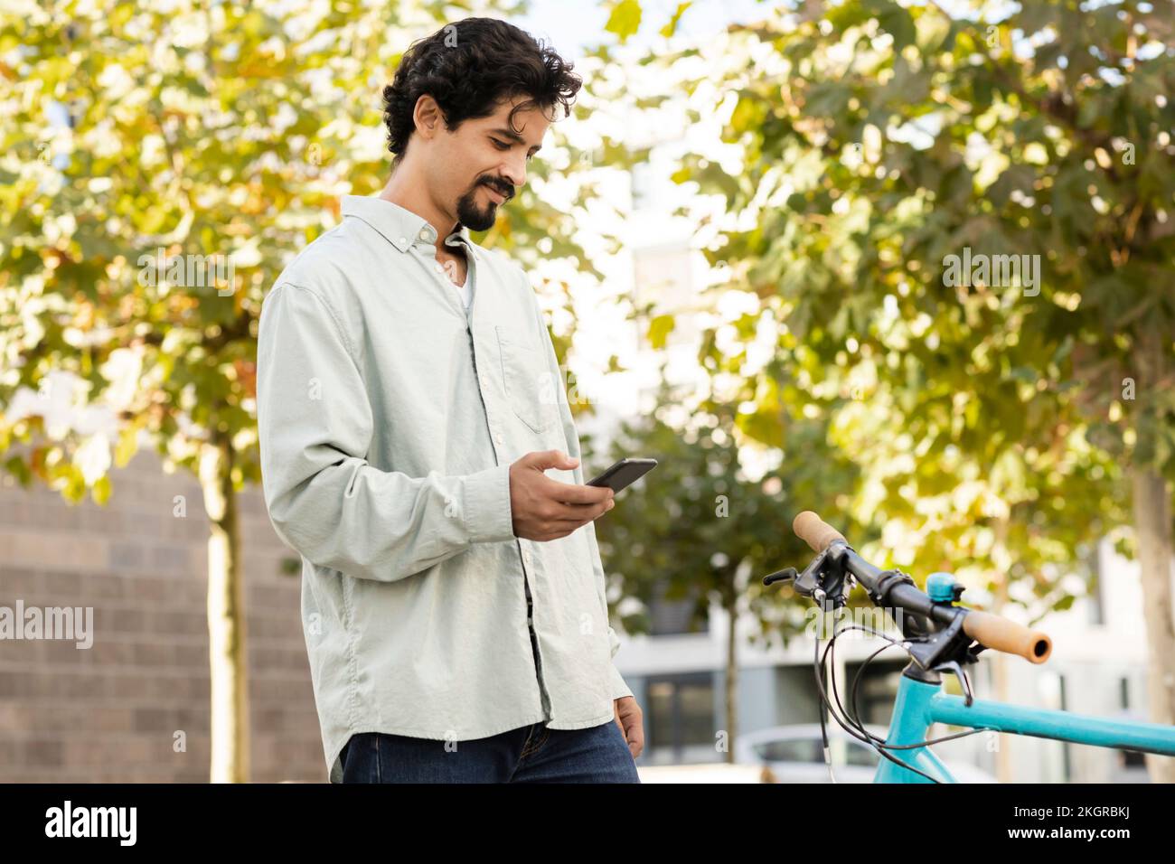 Smiling man using smart phone standing near bicycle Stock Photo