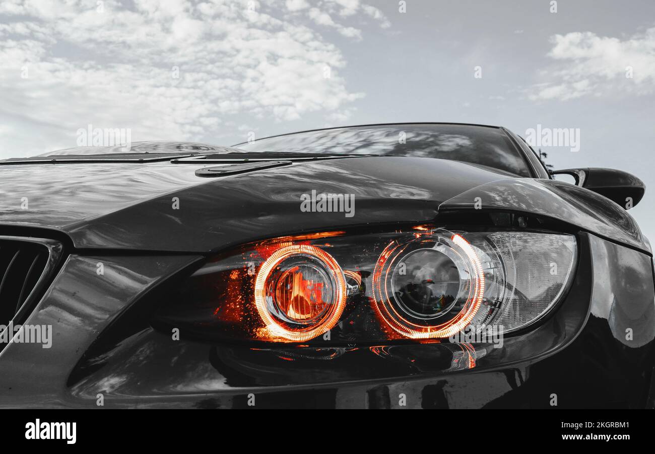 A closeup of a BMW M3 race car with a gray sky and orange headlights ...