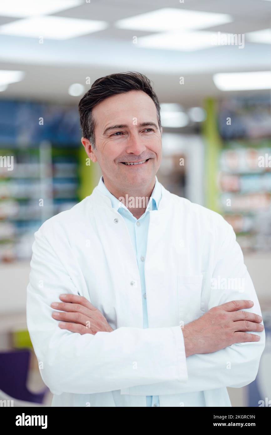 Happy pharmacist with arms crossed in pharmacy Stock Photo