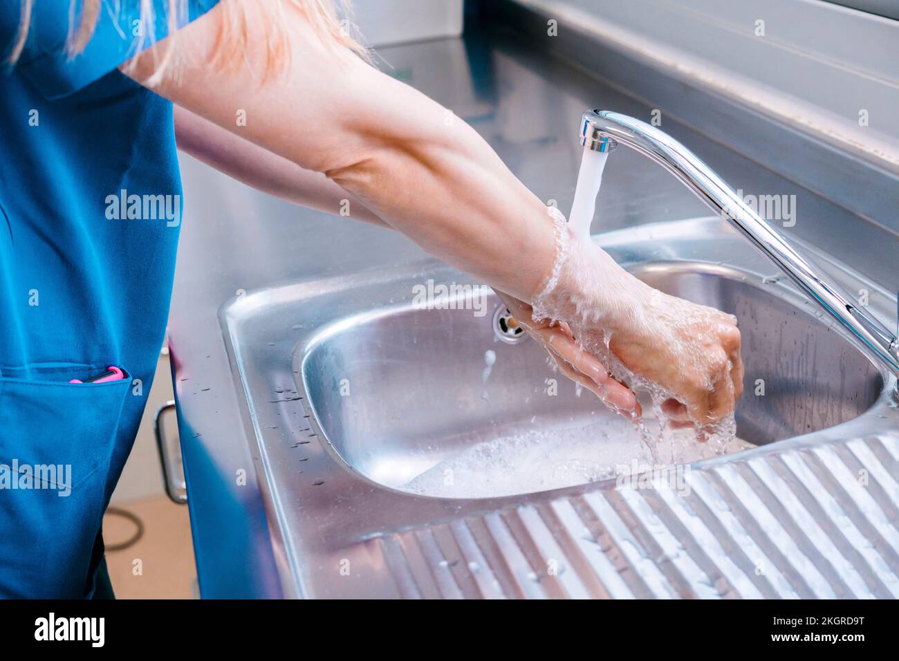 Nurse washing hands with water in sink at hospital Stock Photo