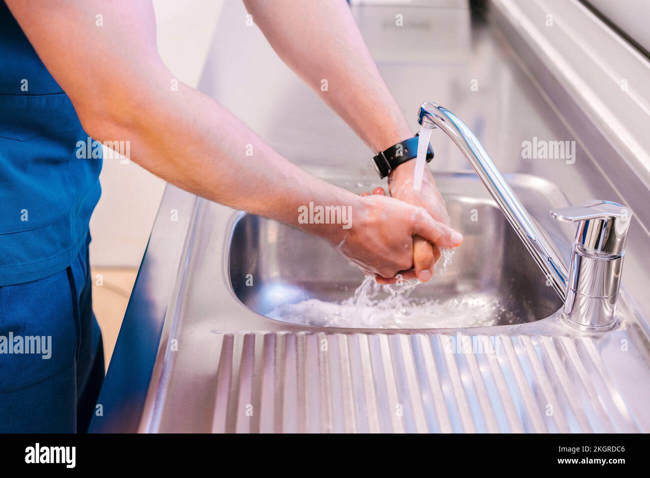 Young doctor washing hands with water in sink at hospital Stock Photo