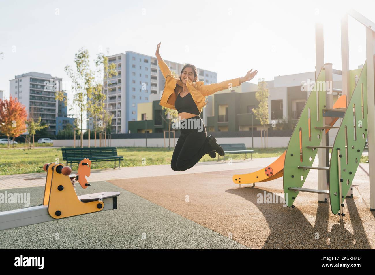 Cheerful woman jumping at playground on sunny day Stock Photo
