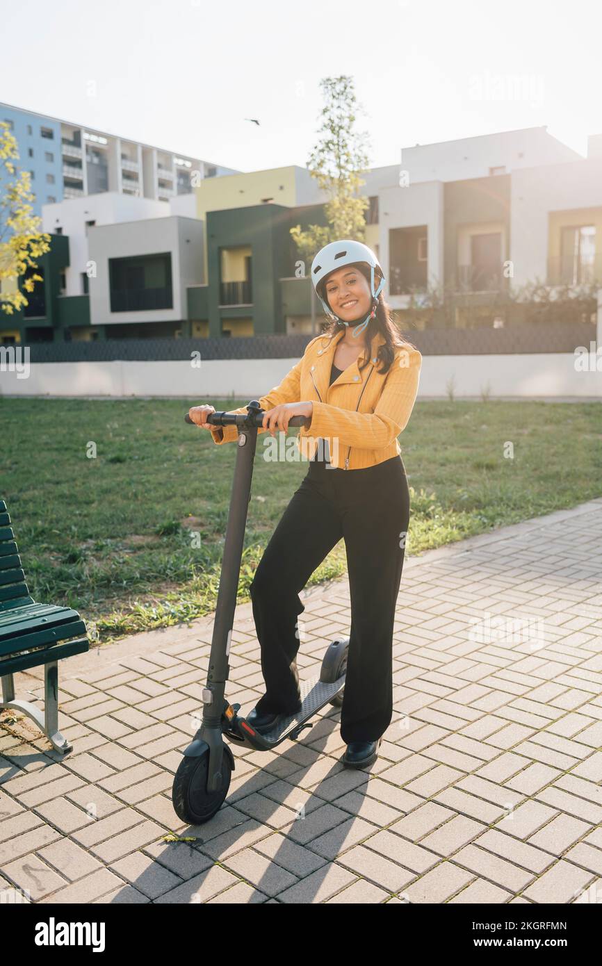 Happy young woman standing with electric push scooter on sunny day Stock Photo