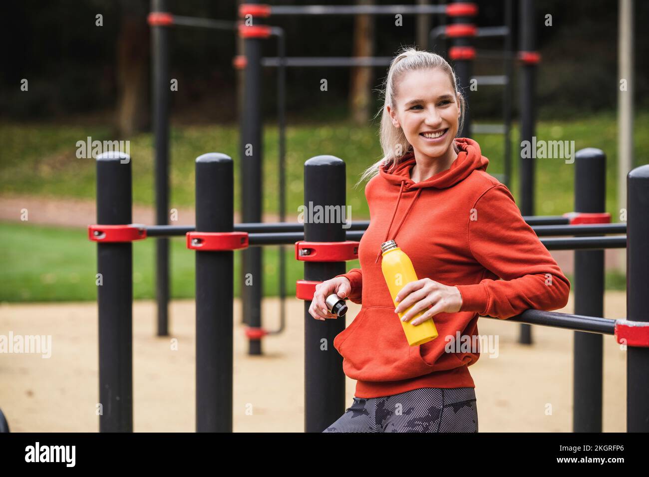 Happy sportswoman holding water bottle leaning on horizontal bar Stock ...