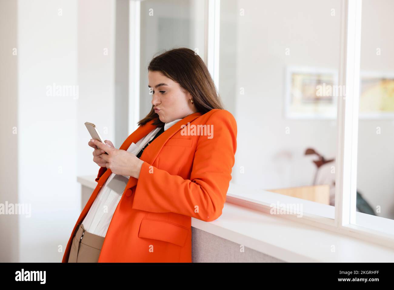 Businesswoman using smart phone leaning on cabinet in office Stock Photo