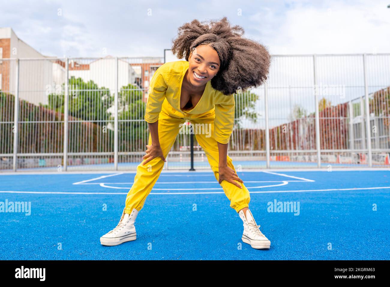 Happy young woman with Afro hairstyle bending on sports court Stock Photo