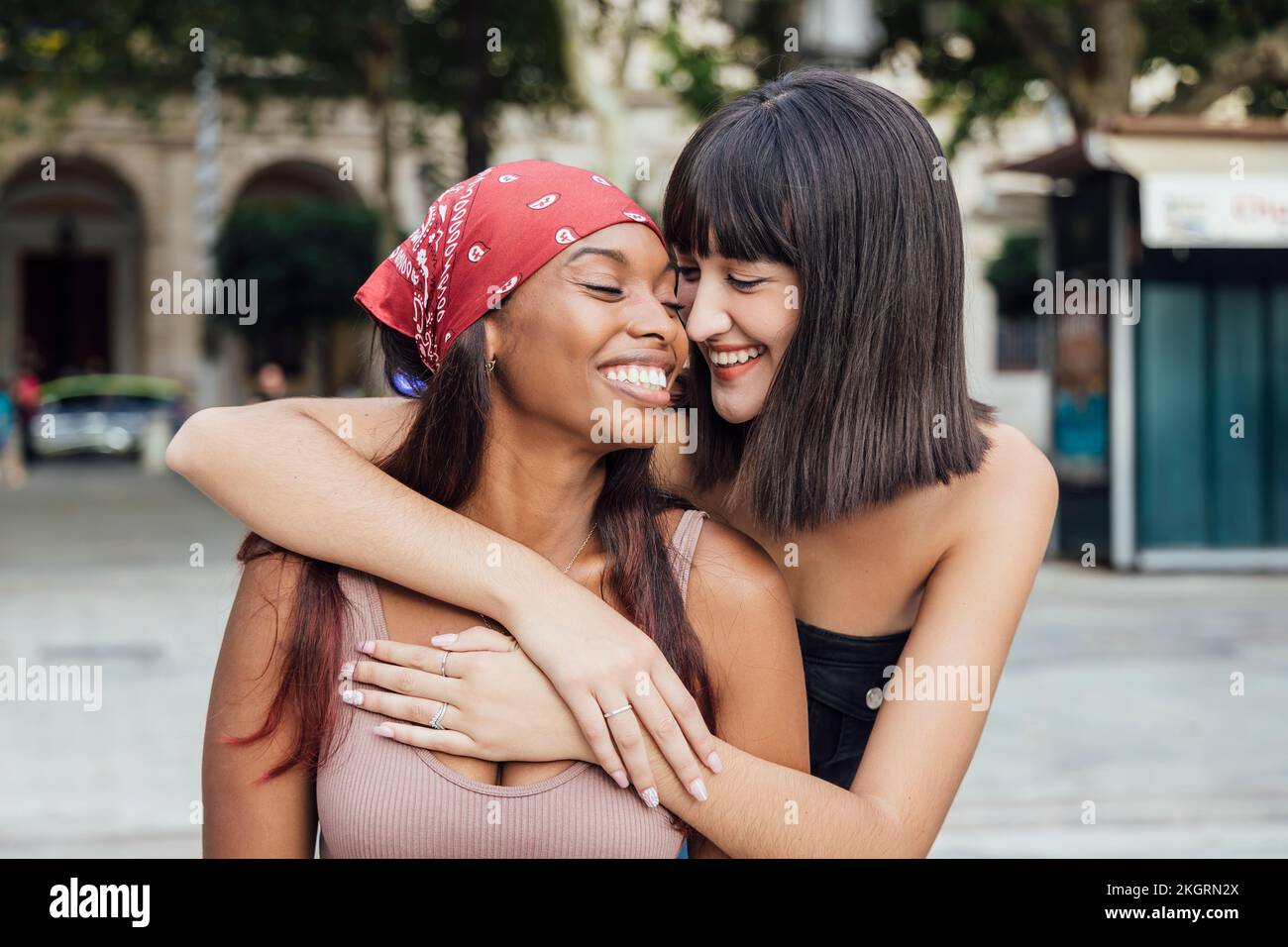 Smiling young woman embracing friend on footpath Stock Photo