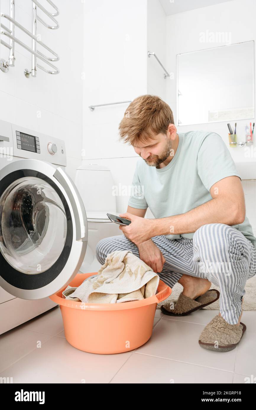 Man using smart phone by washing machine in bathroom at home Stock Photo