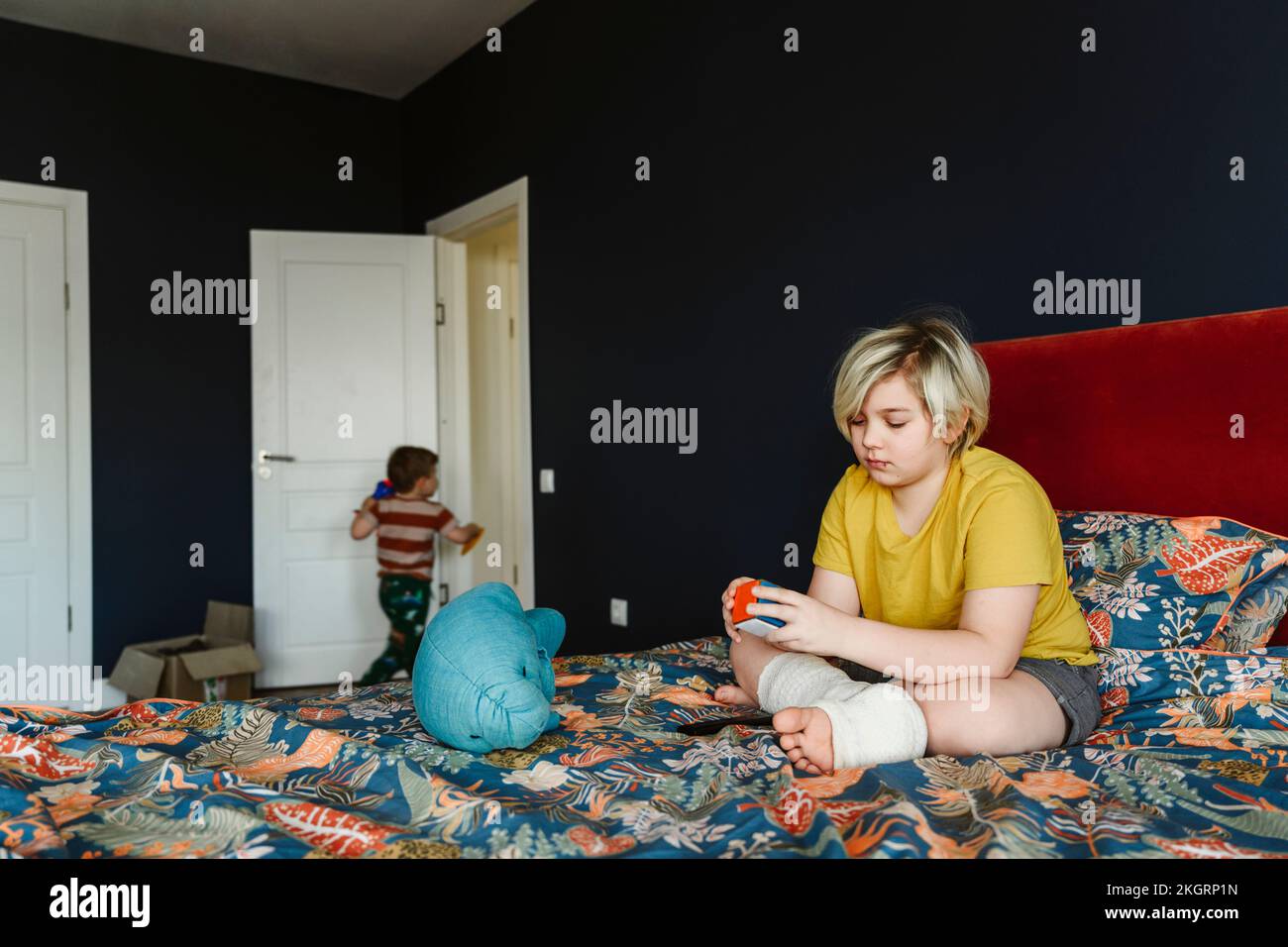 Boy with plaster cast on leg playing with puzzle cube sitting on bed at home Stock Photo