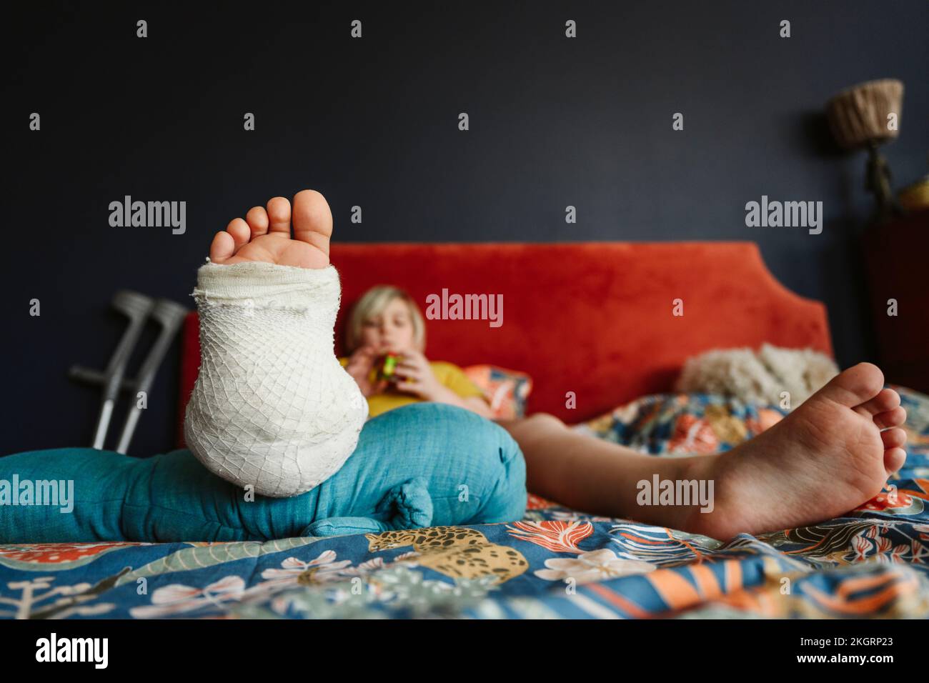 Boy with plaster cast on leg resting on bed at home Stock Photo