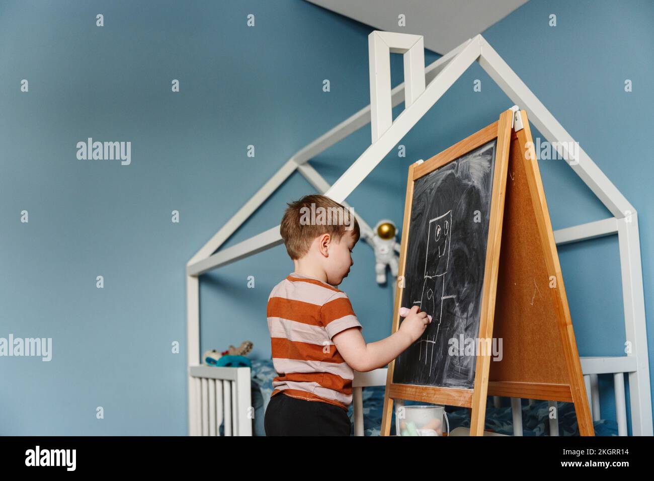 Boy writing on chalkboard in bedroom at home Stock Photo
