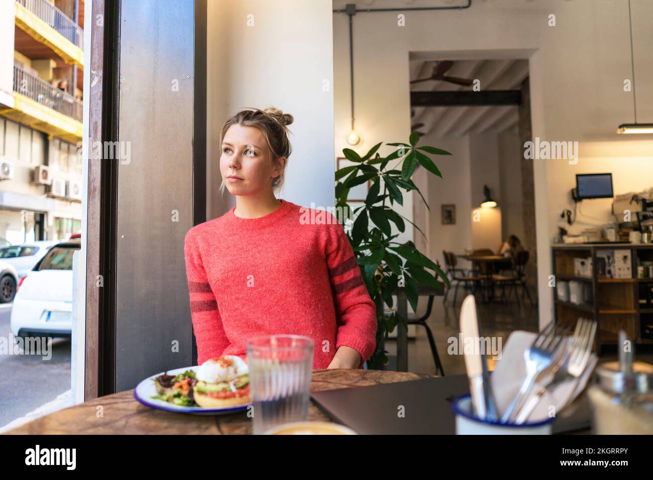 Young freelancer with meal at table looking through window in cafe Stock Photo