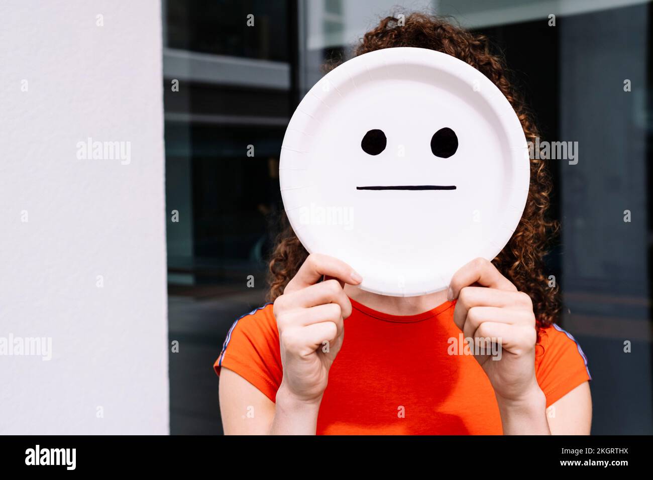 Young woman holding straight smiley emoticon plate over face Stock Photo