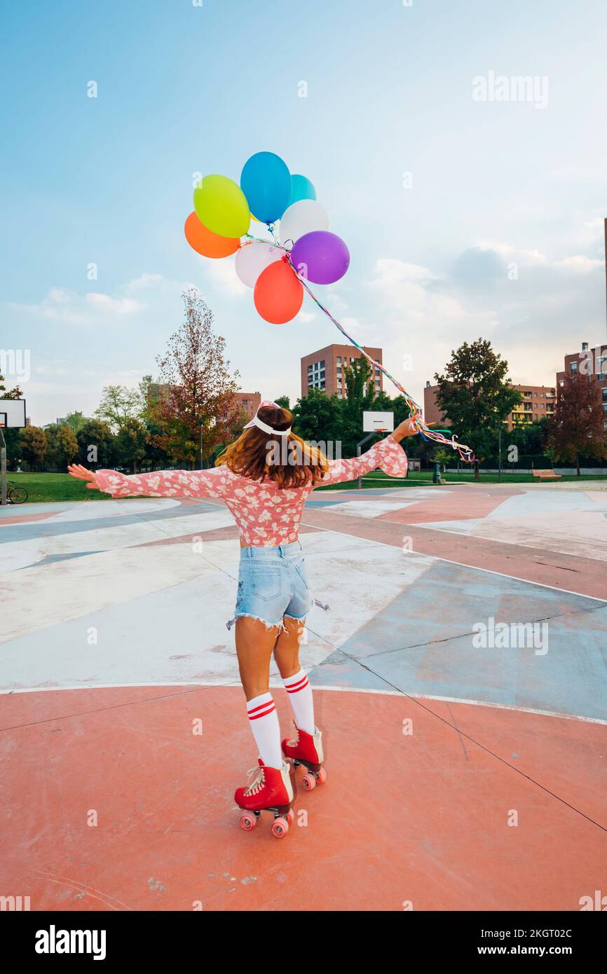 Woman with arms outstretched holding balloons roller skating at sports court Stock Photo