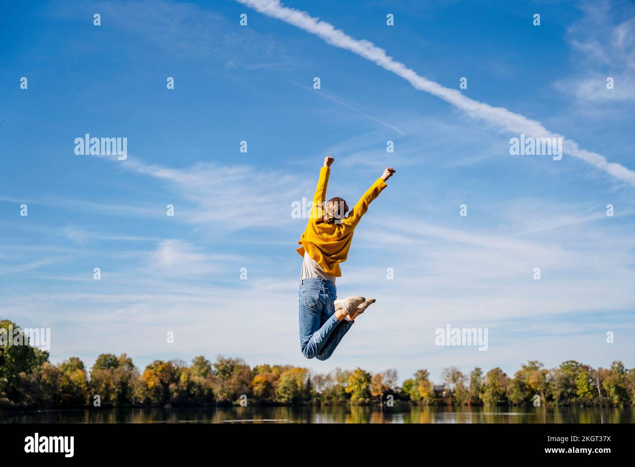 Woman with arms raised jumping under sky Stock Photo