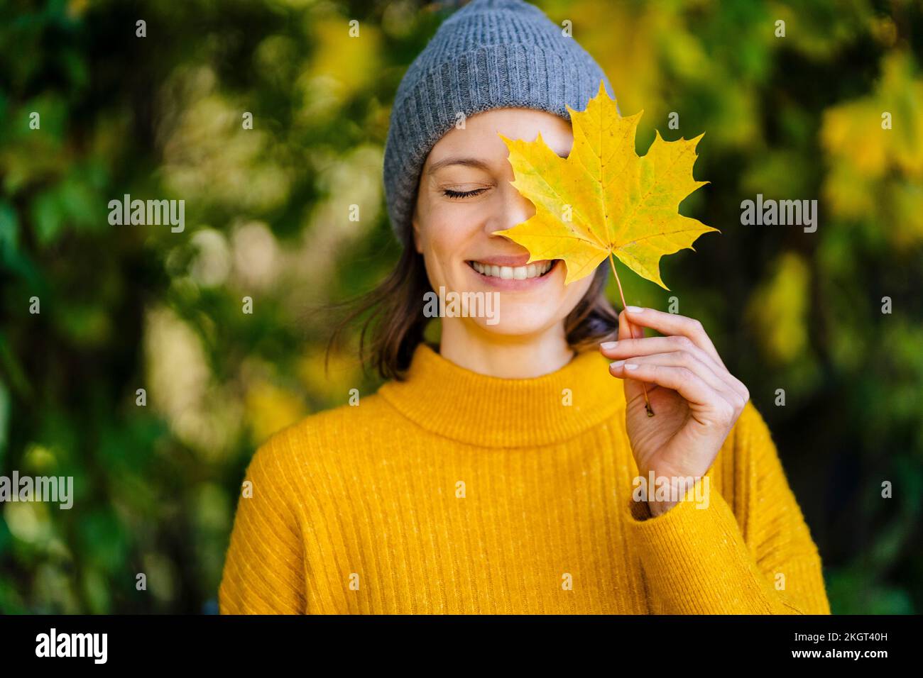 Happy woman holding yellow maple leaf over face Stock Photo