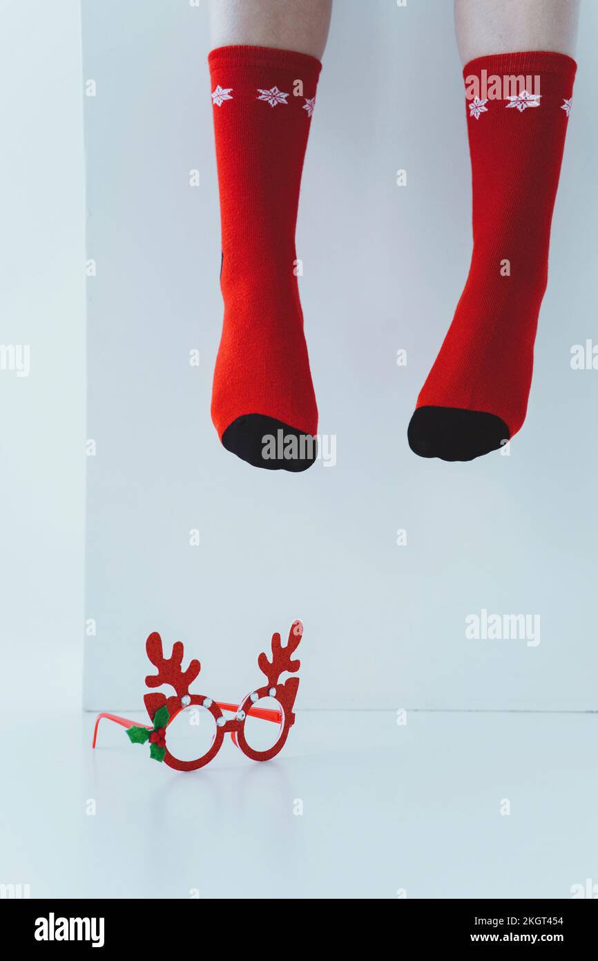 Legs of girl wearing red Christmas socks with reindeer antler glasses on white floor Stock Photo