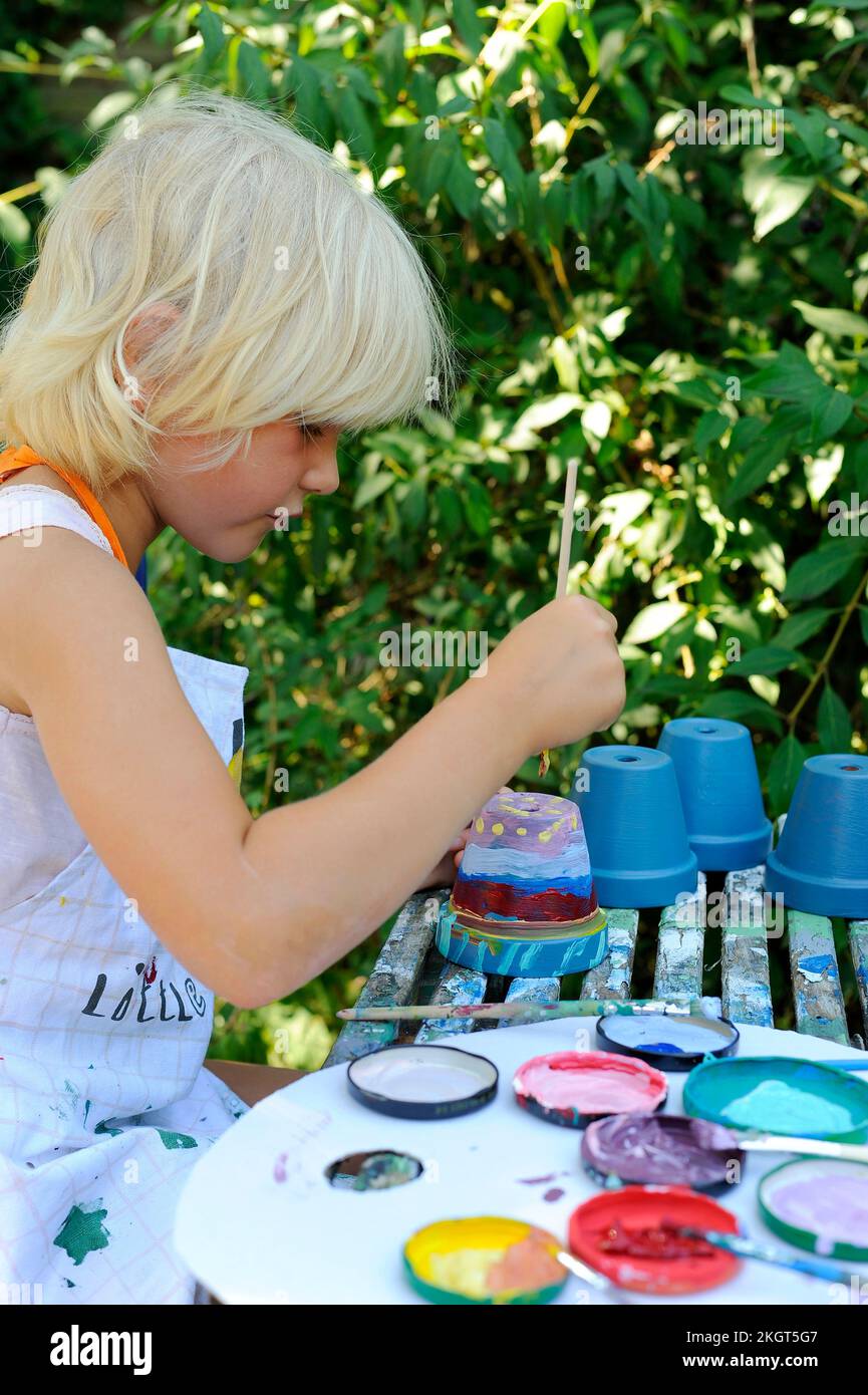 Little girl painting flower pots in garden Stock Photo