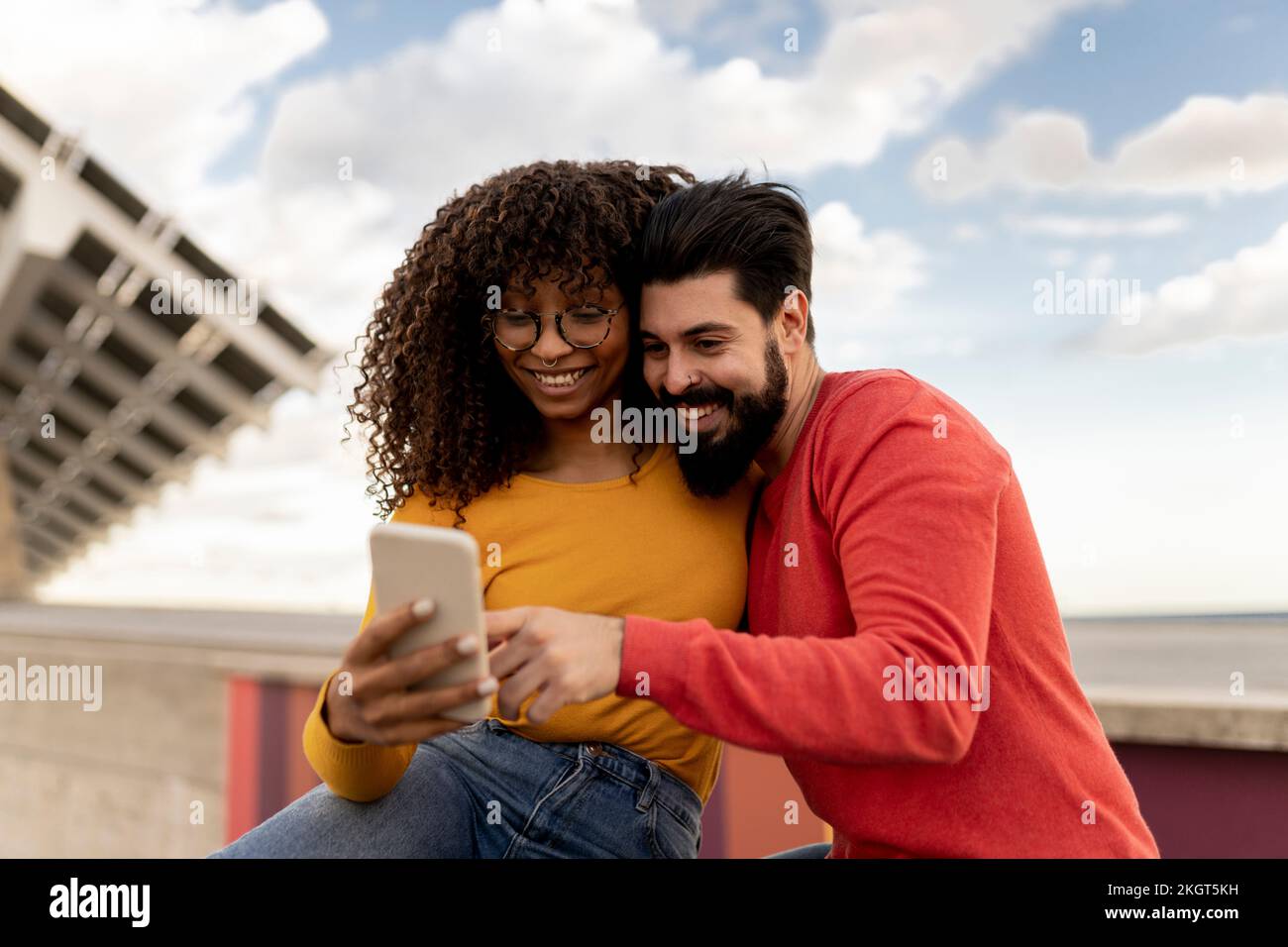 Happy young couple using smart phone under cloudy sky Stock Photo