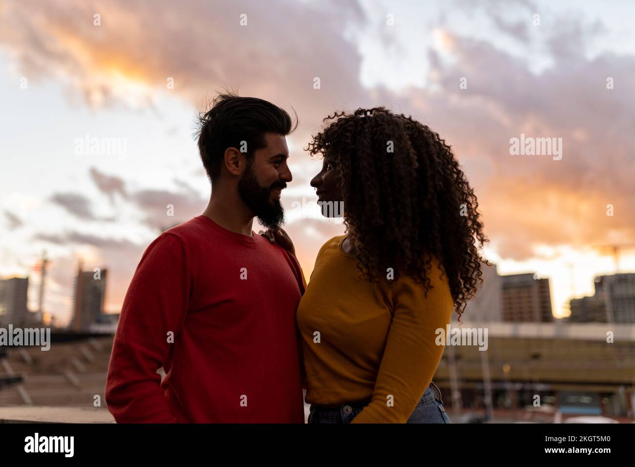 Happy young couple standing under sky at sunset Stock Photo