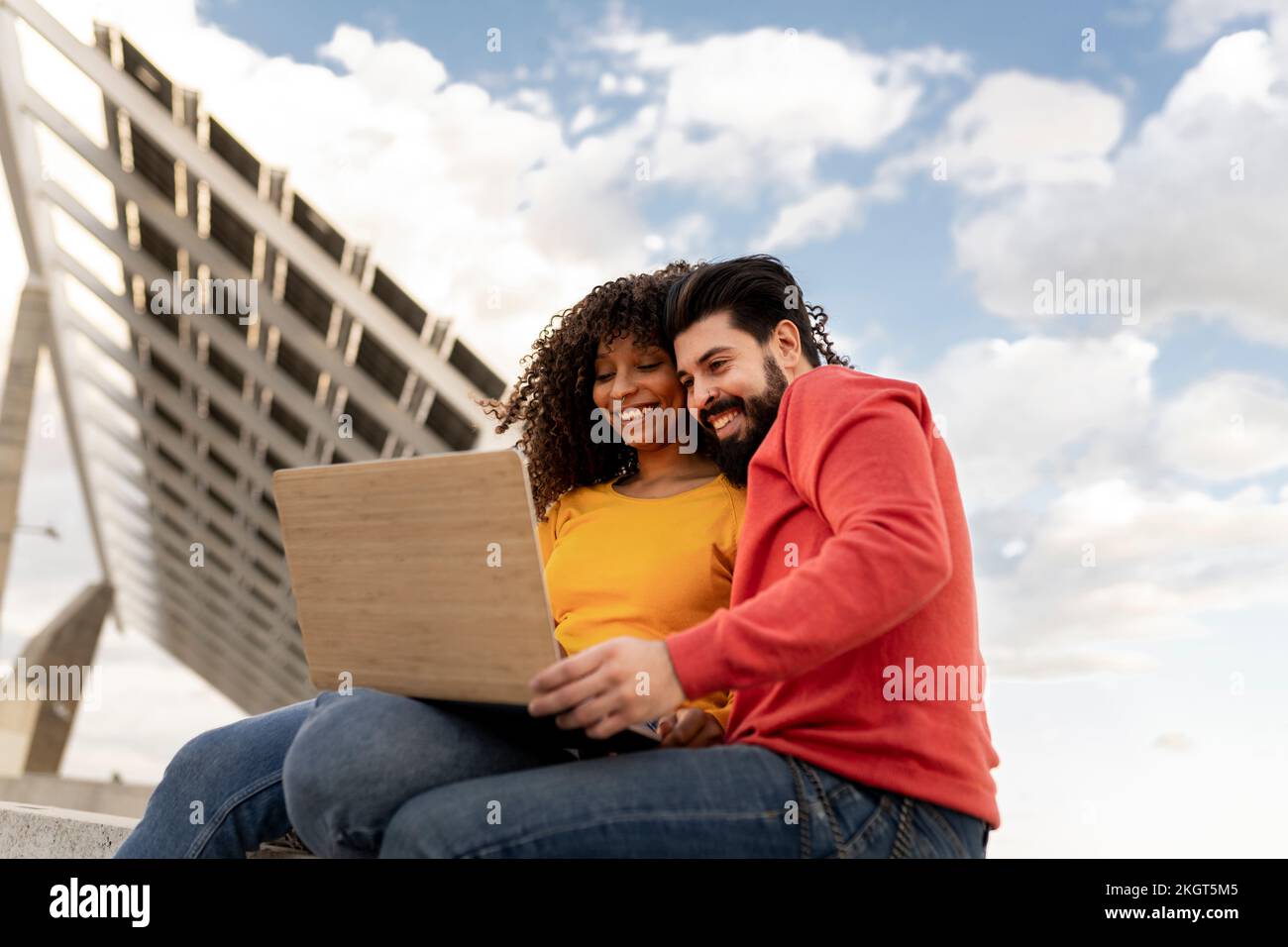 Happy young couple using laptop under cloudy sky Stock Photo