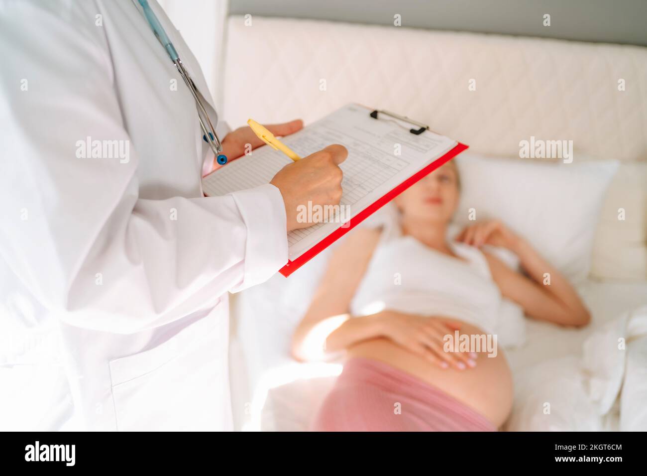 Doctor writing prescription with pregnant woman lying on bed Stock