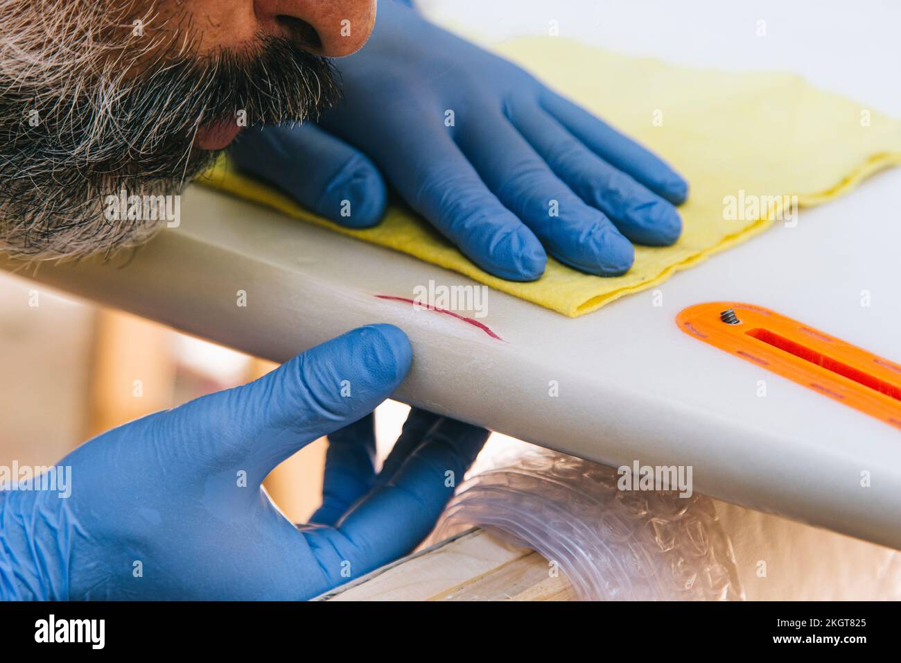 A closeup of a bearded surfer repairing a damaged part of a surfboard Stock Photo