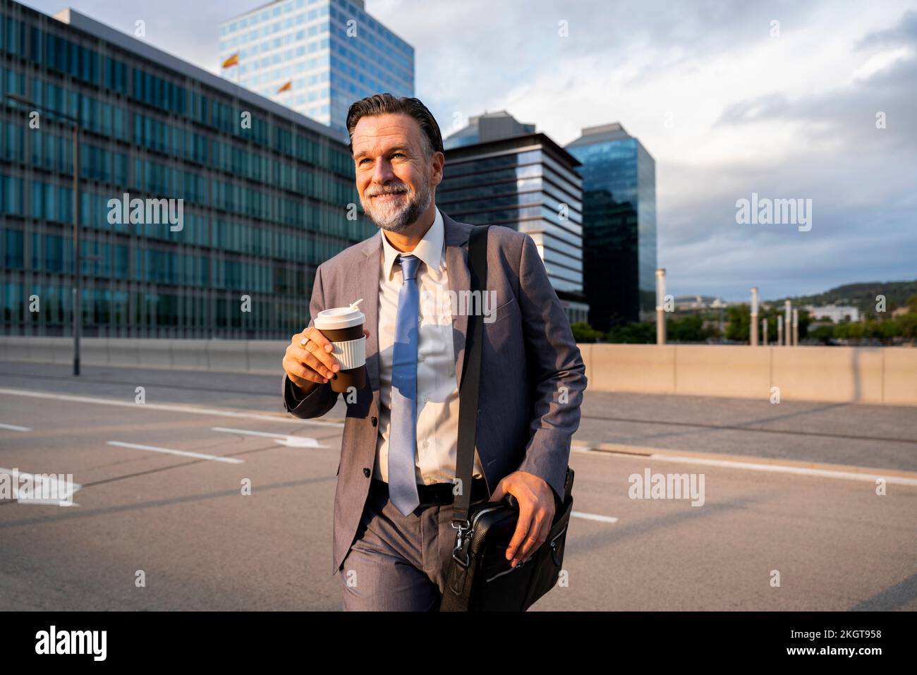 Smiling mature businessman holding disposable coffee cup walking on street Stock Photo