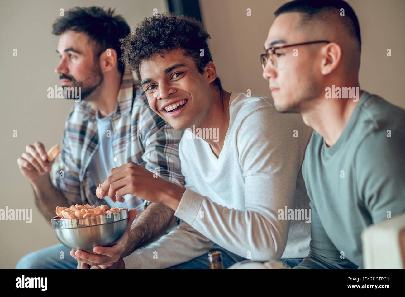 Merry guy snacking on chips in presence of his pals Stock Photo